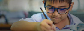 Young boy with glasses writing